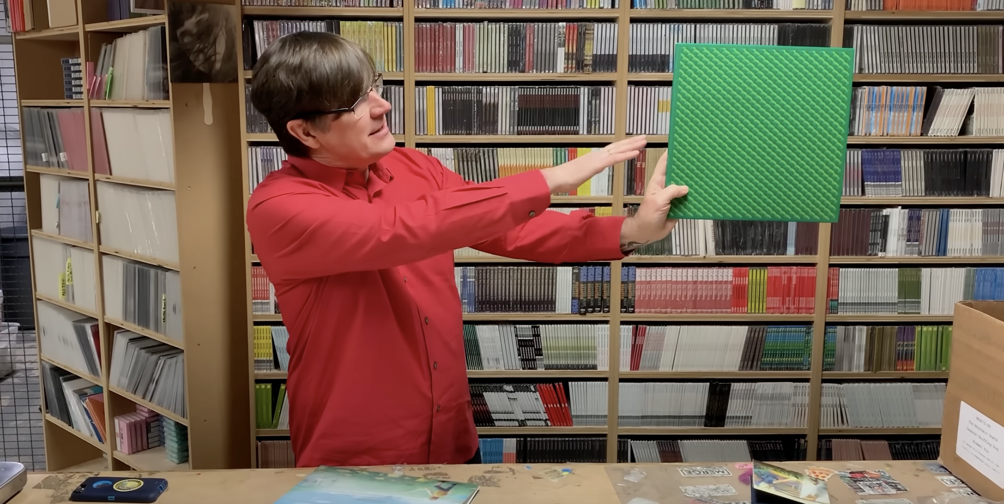 John Darnielle of the Mountain Goats holding up a limited edition LP of In League with Dragons with a shiny green slipcase that mimics dragon scales.