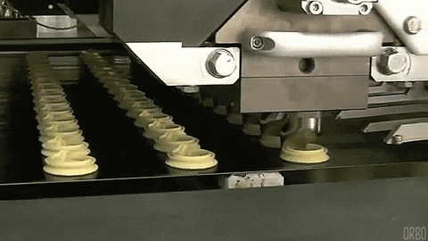 A robot creates multiple cookie swirls on a conveyor belt.