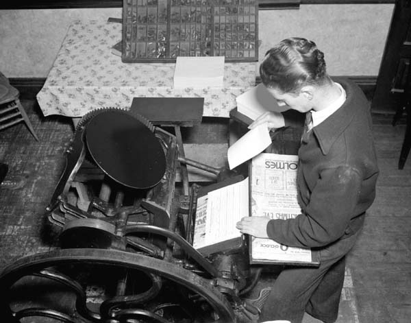 1930s black and white image of a man using a printing press.
